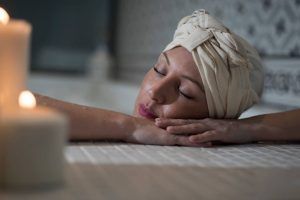 En Le Patio Spa, una persona disfruta de un Ritual Básico con exfoliación, con los ojos cerrados y la cabeza envuelta en una toalla, descansando sobre los brazos cruzados junto a velas encendidas para una relajación máxima. - ForTwo - Planes para parejas