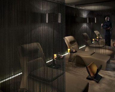 En el Mandarin Hotel en Barcelona SPA, una iluminación tenue crea un ambiente tranquilo con sillones elegantemente separados por cortinas oscuras y una figura serena en silencio al fondo. - ForTwo - Planes para parejas