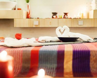 En Magic Experience Urban Spa 1850 Barcelona, disfruta de la relajación con toallas dobladas en forma de corazón sobre una mesa de rayas vibrantes en medio del suave resplandor de las velas y una iluminación tenue. - ForTwo - Planes para parejas