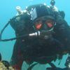 Un buceador, completamente equipado con equipo de buceo, disfruta de la emoción de la "Oferta: Bautismo de buceo (Granada)" mientras explora bajo el agua cerca de rocas cubiertas de coral y una vibrante vida marina. - ForTwo - Planes para parejas