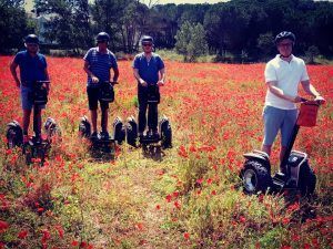 Cuatro personas se deslizan por un campo de amapolas rojas en la Ruta en Segway en los arrozales de Pals, ataviadas con cascos y ropa informal de verano. - ForTwo - Planes para parejas