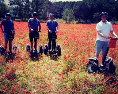 Cuatro personas se deslizan por un campo de amapolas rojas en la Ruta en Segway en los arrozales de Pals, ataviadas con cascos y ropa informal de verano. - ForTwo - Planes para parejas