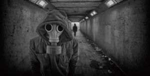 En el túnel poco iluminado, una persona con una máscara de gas permanece tensa, haciendo eco de la atmósfera misteriosa de Lanzadera Alien - Un juego de The Resistance Escape Room (Barcelona), mientras otra figura se acerca a lo lejos. - ForTwo - Planes para parejas