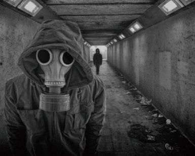 En el túnel poco iluminado, una persona con una máscara de gas permanece tensa, haciendo eco de la atmósfera misteriosa de Lanzadera Alien - Un juego de The Resistance Escape Room (Barcelona), mientras otra figura se acerca a lo lejos. - ForTwo - Planes para parejas