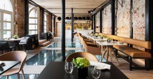 El Restaurante Dos Cielos en Madrid presume de un interior moderno con suelo de cristal, paredes de ladrillo y una elegante iluminación. Las mesas están elegantemente dispuestas con copas y plantas verdes, creando un ambiente refrescante. - ForTwo - Planes para parejas