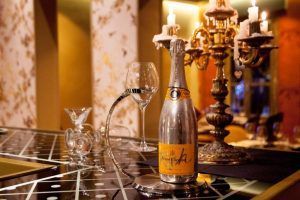 Una botella y una copa de champán de Un Restaurante Küche (Madrid) adornan una mesa elegante, con velas en un candelabro ornamentado que proyectan un brillo cálido, creando un ambiente lujoso similar a una experiencia gastronómica de lujo. - ForTwo - Planes para parejas