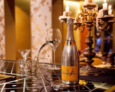 Una botella y una copa de champán de Un Restaurante Küche (Madrid) adornan una mesa elegante, con velas en un candelabro ornamentado que proyectan un brillo cálido, creando un ambiente lujoso similar a una experiencia gastronómica de lujo. - ForTwo - Planes para parejas