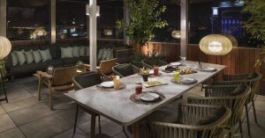Restaurante Radio ME, situado en la azotea del Hotel Meliá Madrid, ofrece un elegante comedor al aire libre con una mesa para cuatro con asientos con cojines verdes e iluminación ambiental que crea una atmósfera nocturna mágica. - ForTwo - Planes para parejas