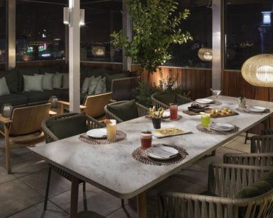 Restaurante Radio ME, situado en la azotea del Hotel Meliá Madrid, ofrece un elegante comedor al aire libre con una mesa para cuatro con asientos con cojines verdes e iluminación ambiental que crea una atmósfera nocturna mágica. - ForTwo - Planes para parejas