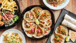 Una variedad de platos mexicanos, incluyendo tacos, papas fritas y ensalada, bellamente dispuestos en una mesa de madera en el Restaurante Mexicano Mr. Uchu en Santander. - ForTwo - Planes para parejas