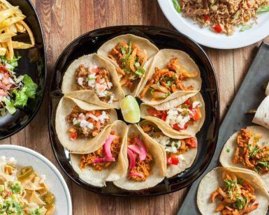 Una variedad de platos mexicanos, incluyendo tacos, papas fritas y ensalada, bellamente dispuestos en una mesa de madera en el Restaurante Mexicano Mr. Uchu en Santander. - ForTwo - Planes para parejas