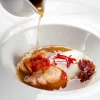 Disfrute de un menú degustación con estrella Michelin en el Restaurante Nectari de Barcelona, que incluye un plato gourmet de huevo escalfado, camarones y jamón en un caldo rico servido en un tazón blanco impecable. - ForTwo - Planes para parejas