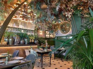 El restaurante Purnima en Madrid, con exuberante vegetación, una decoración elegante, un espejo circular y mesas bien dispuestas, ofrece un entorno tranquilo para saborear el menú de degustación de cocina india. - ForTwo - Planes para parejas