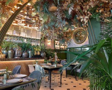 El restaurante Purnima en Madrid, con exuberante vegetación, una decoración elegante, un espejo circular y mesas bien dispuestas, ofrece un entorno tranquilo para saborear el menú de degustación de cocina india. - ForTwo - Planes para parejas