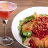 Una ensalada vibrante cubierta con frutos rojos complementa un cóctel rosa en una copa de martini, seduciendo a los comensales del Restaurante La Cocotte Cocina internacional en Málaga, todo elegantemente dispuesto en una encantadora mesa de madera. - ForTwo - Planes para parejas