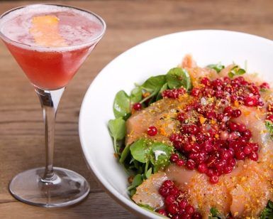 Una ensalada vibrante cubierta con frutos rojos complementa un cóctel rosa en una copa de martini, seduciendo a los comensales del Restaurante La Cocotte Cocina internacional en Málaga, todo elegantemente dispuesto en una encantadora mesa de madera. - ForTwo - Planes para parejas