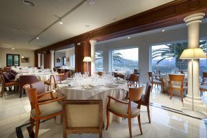El Menú romántico en el restaurante Abades (Ronda) ofrece una experiencia gastronómica inolvidable con elegantes mesas redondas, sillas de madera, manteles blancos y grandes ventanales que muestran cautivadoras vistas a las palmeras. - ForTwo - Planes para parejas