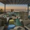 La Cena Romántica con vistas en la azotea El Llorenç de Palma de Mallorca ofrece un entorno romántico con asientos acogedores, vistas al mar al atardecer y muebles tejidos adornados con cojines neutros y verde azulado. - ForTwo - Planes para parejas