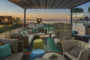 La Cena Romántica con vistas en la azotea El Llorenç de Palma de Mallorca ofrece un entorno romántico con asientos acogedores, vistas al mar al atardecer y muebles tejidos adornados con cojines neutros y verde azulado. - ForTwo - Planes para parejas