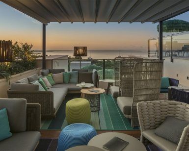 La Cena Romántica con vistas en la azotea El Llorenç de Palma de Mallorca ofrece un entorno romántico con asientos acogedores, vistas al mar al atardecer y muebles tejidos adornados con cojines neutros y verde azulado. - ForTwo - Planes para parejas