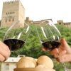 En el Restaurante Ruta del Azafrán, dos personas chocan copas de vino con panecillos mientras disfrutan del Menú Sabores en Restaurante Ruta del Azafrán frente a la Alhambra, con la histórica Alhambra majestuosa al fondo. - ForTwo - Planes para parejas