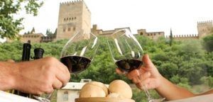 En el Restaurante Ruta del Azafrán, dos personas chocan copas de vino con panecillos mientras disfrutan del Menú Sabores en Restaurante Ruta del Azafrán frente a la Alhambra, con la histórica Alhambra majestuosa al fondo. - ForTwo - Planes para parejas