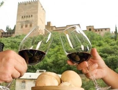 En el Restaurante Ruta del Azafrán, dos personas chocan copas de vino con panecillos mientras disfrutan del Menú Sabores en Restaurante Ruta del Azafrán frente a la Alhambra, con la histórica Alhambra majestuosa al fondo. - ForTwo - Planes para parejas