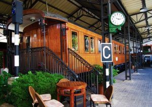 El Restaurante El Vagón de Beni en Madrid ofrece una experiencia gastronómica única en un antiguo vagón de tren transformado en cafetería. Disfrute de sus comidas rodeado de mesas, sillas, exuberante vegetación y un reloj en el techo en este encantador entorno que evoca el ambiente de un restaurante tradicional. - ForTwo - Planes para parejas