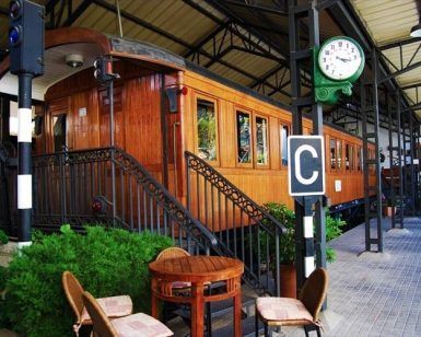 El Restaurante El Vagón de Beni en Madrid ofrece una experiencia gastronómica única en un antiguo vagón de tren transformado en cafetería. Disfrute de sus comidas rodeado de mesas, sillas, exuberante vegetación y un reloj en el techo en este encantador entorno que evoca el ambiente de un restaurante tradicional. - ForTwo - Planes para parejas