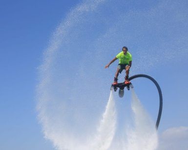 Flotando en las cristalinas aguas de Barcelona, una persona en "Vuela sobre el agua en Hoverboard o Flyboard en Barcelona" crea un patrón circular de rociado contra el cielo azul claro. - ForTwo - Planes para parejas
