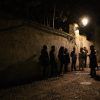 Un grupo se reúne en un callejón poco iluminado del Albaicín, iluminado por una farola, mientras su guía, con sombrero, comparte apasionadamente las historias ocultas de Granada en el Tour Conspiración en el Albaicín Granada. - ForTwo - Planes para parejas