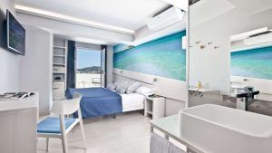 Disfrute de una habitación moderna en el Escapada Hotel Ryans La Marina con cama doble, detalles en azul, obras de arte playeras y balcón con vistas al mar. Disfrute del ambiente ibicenco con desayuno incluido para empezar el día. - ForTwo - Planes para parejas