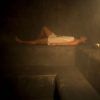 Envuelta en una toalla, la persona se sienta serenamente en un banco de piedra en la sala de vapor tenuemente iluminada de Rituels d'Orient Barcelona, abrazando el ambiente tranquilo que recuerda al Hammam Ritual de los Sultanes. - ForTwo - Planes para parejas