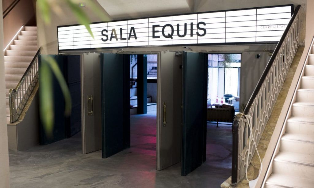 El Hotel Vincci Gala de Barcelona cuenta con un moderno salón con cómodos asientos, cojines coloridos e iluminación contemporánea. Un elegante bar complementa las vibrantes estanterías rojas, representando el ambiente chic de la ciudad. - ForTwo - Planes para parejas