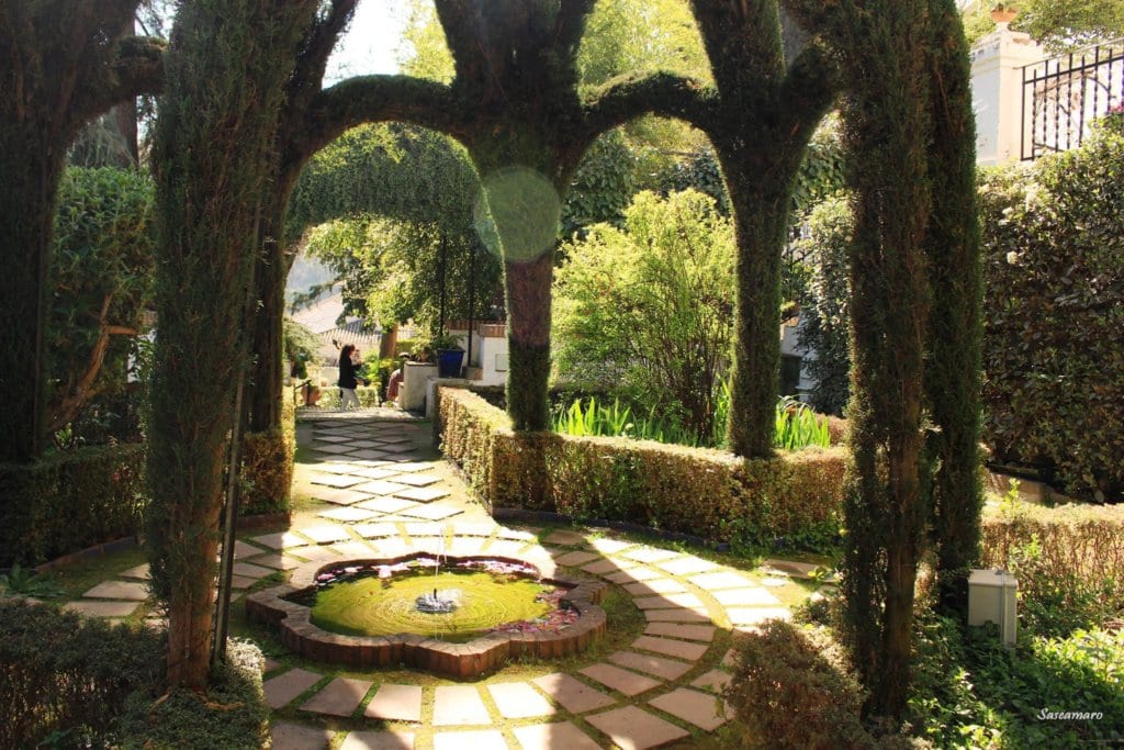 Este jardín, como una joya escondida que recuerda al encantador barrio del Albaicín de Granada, cuenta con una estructura de seto arqueada, una fuente circular y un camino de piedra rodeado de exuberante vegetación: una escapada tranquila similar a la experiencia de la Visita al Albaicín y Sacromonte. - ForTwo - Planes para parejas