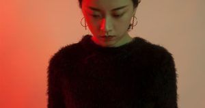 En IM Estudio de Madrid, bajo una dramática iluminación roja y verde, una mujer que viste un suéter negro peludo y pendientes de aro mira hacia abajo en una impactante fotografía de estudio. - ForTwo - Planes para parejas