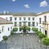 El patio del Hotel de 4 estrellas Hospes Las Casas del Rey Baeza en Sevilla cuenta con árboles simétricos, un techo de tejas y un cielo azul claro, creando un oasis de relajación. - ForTwo - Planes para parejas