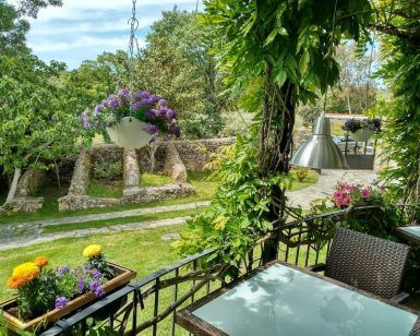 Mesas, plantas colgantes y flores crean un encantador patio con jardín contra una pared de piedra rústica, capturando la esencia tranquila de Almazara de San Pedro - Casa rural en Sierra de Gata con baño árabe (Cáceres), con exuberante vegetación para una escena encantadora. - ForTwo - Planes para parejas