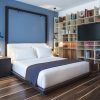 Crea un dormitorio moderno inspirado en el Hotel Sir Joan de Ibiza, con una pared con acento azul, pisos de madera, estantes elegantes y una cama acogedora vestida con sábanas blancas y una manta oscura. - ForTwo - Planes para parejas
