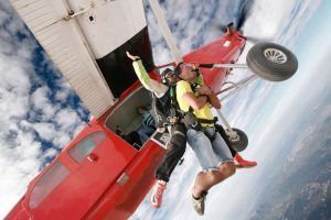 Dos personas saltan en paracaidismo en tándem desde un avión rojo, con el cielo azul expansivo y las nubes como telón de fondo: una experiencia Paracaidismo en Barcelona desde 4000 metros - BCN SkyDive impresionante. - ForTwo - Planes para parejas