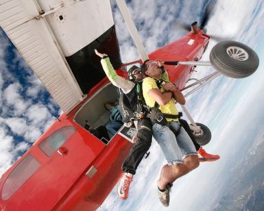Dos personas saltan en paracaidismo en tándem desde un avión rojo, con el cielo azul expansivo y las nubes como telón de fondo: una experiencia Paracaidismo en Barcelona desde 4000 metros - BCN SkyDive impresionante. - ForTwo - Planes para parejas