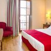 Experimente la comodidad y el estilo en Escapada Hotel Soho Boutique Casa Don Fernando, Cáceres. Disfrute de una acogedora habitación con cama doble, manta roja, silla, escritorio, televisión y balcón con cortinas de rayas. Incluye desayuno, cata de ibéricos y vino en el corazón de la ciudad. - ForTwo - Planes para parejas