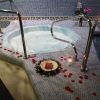 El Spa para 2 personas con masaje relajante opcional en Aquabody Wellness & SPA (Madrid) ofrece un lujoso jacuzzi para dos, adornado con pétalos de rosa y velas para un ambiente perfecto, complementado con un libro en una corona en esta serena sala de spa con azulejos. - ForTwo - Planes para parejas