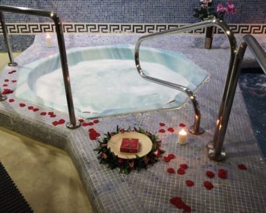 El Spa para 2 personas con masaje relajante opcional en Aquabody Wellness & SPA (Madrid) ofrece un lujoso jacuzzi para dos, adornado con pétalos de rosa y velas para un ambiente perfecto, complementado con un libro en una corona en esta serena sala de spa con azulejos. - ForTwo - Planes para parejas
