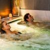 Dos personas disfrutando de un burbujeante jacuzzi en Balneario Areatza, rodeados de velas encendidas y piedras, creando una atmósfera relajante similar al Circuito Termal y Masaje Para Dos en Balneario Areatza2 (Bilbao). - ForTwo - Planes para parejas