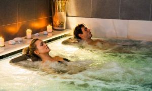 Dos personas disfrutando de un burbujeante jacuzzi en Balneario Areatza, rodeados de velas encendidas y piedras, creando una atmósfera relajante similar al Circuito Termal y Masaje Para Dos en Balneario Areatza2 (Bilbao). - ForTwo - Planes para parejas