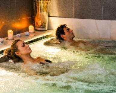 Dos personas disfrutando de un burbujeante jacuzzi en Balneario Areatza, rodeados de velas encendidas y piedras, creando una atmósfera relajante similar al Circuito Termal y Masaje Para Dos en Balneario Areatza2 (Bilbao). - ForTwo - Planes para parejas