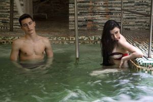 En Termas de Hispalis, una mujer se relaja en el borde de la piscina y un hombre se encuentra en agua tibia, ambos disfrutando de la relajante experiencia del Circuito Termal con Masaje. - ForTwo - Planes para parejas