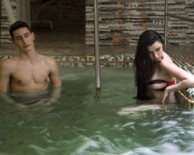 En Termas de Hispalis, una mujer se relaja en el borde de la piscina y un hombre se encuentra en agua tibia, ambos disfrutando de la relajante experiencia del Circuito Termal con Masaje. - ForTwo - Planes para parejas