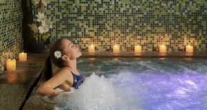 En Barcelona, una mujer se relaja con los ojos cerrados en un jacuzzi de spa, rodeada de velas parpadeantes y mosaicos, disfrutando del ambiente relajante que ofrece el Spa y masaje con velas para dos. - ForTwo - Planes para parejas
